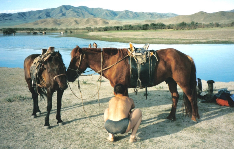 Onafscheidelijk in Mongolië: man en paard jongen met paard bij rivier in Mongolië